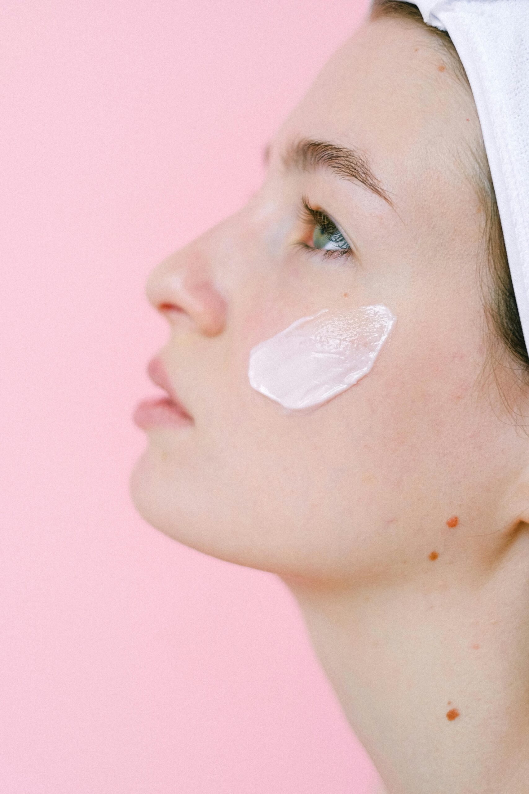 A serene portrait of a woman with facial cream against a pink background.
